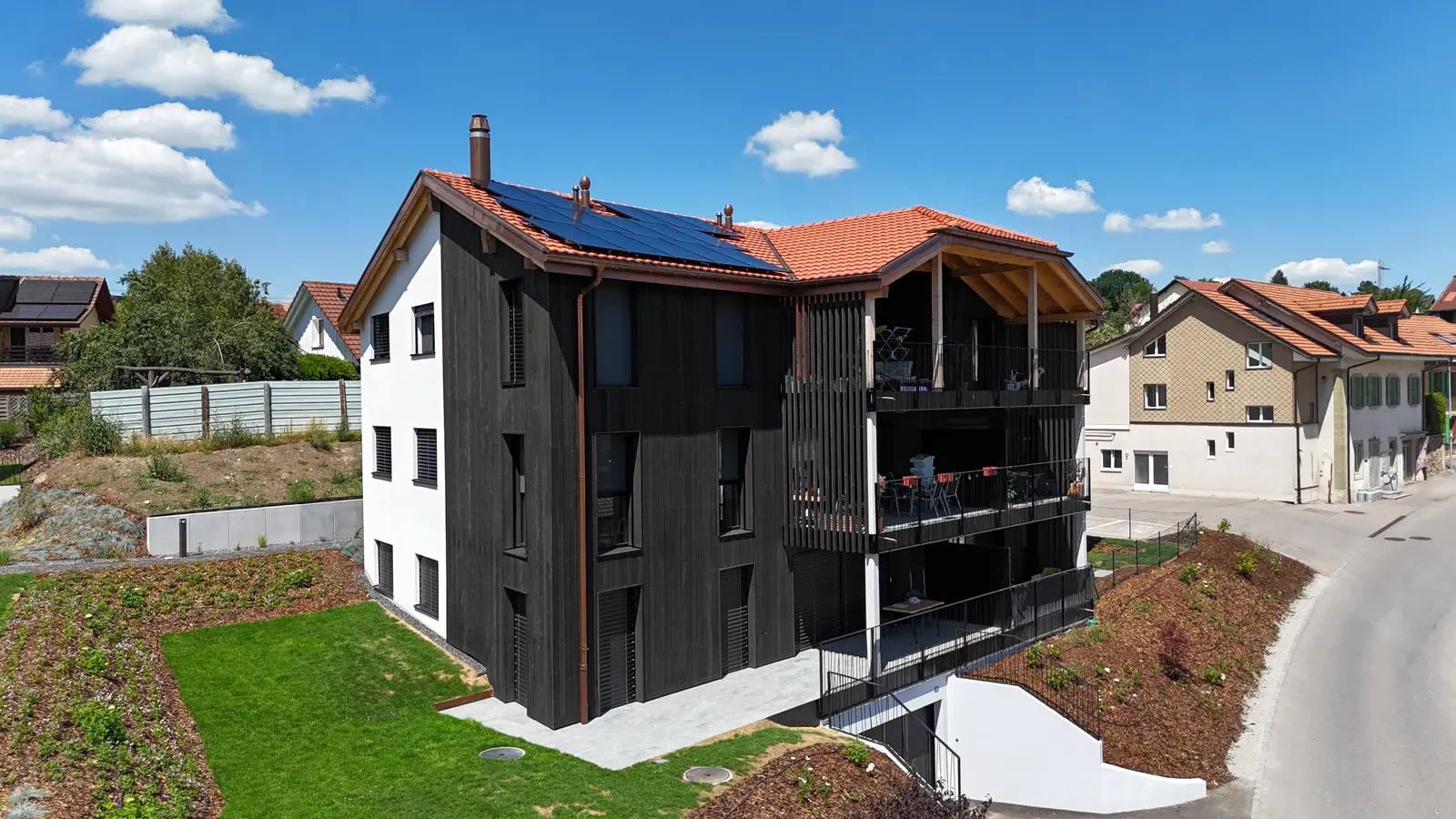Immeuble résidentiel à façade bois foncé et balcons couverts, Cottens